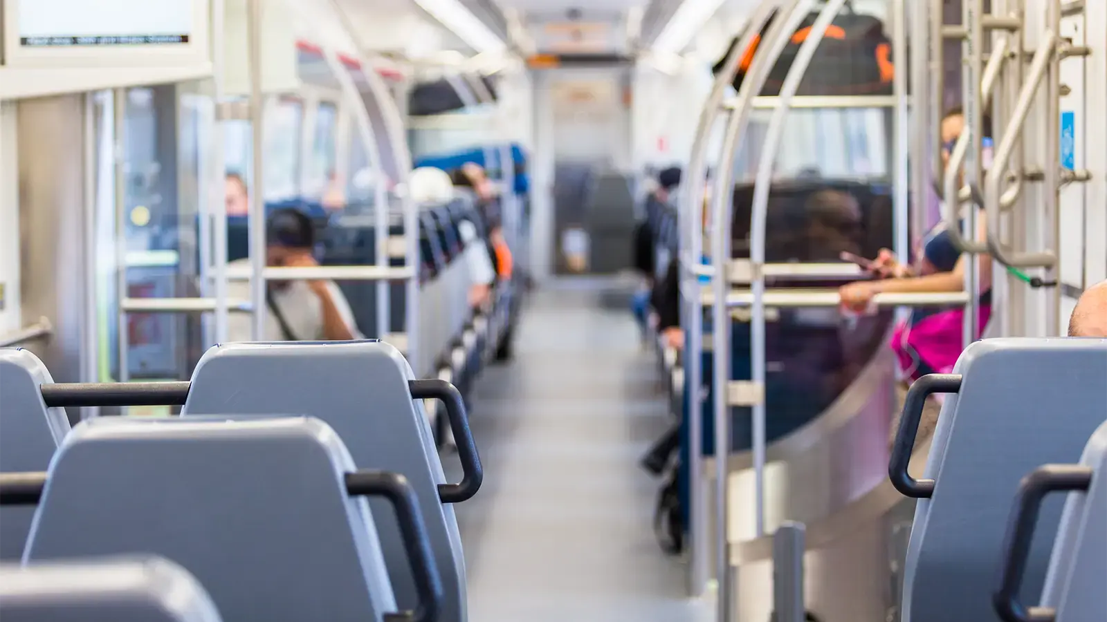 Inside a commuter train car with empty seats in the foreground and a few riders in the background